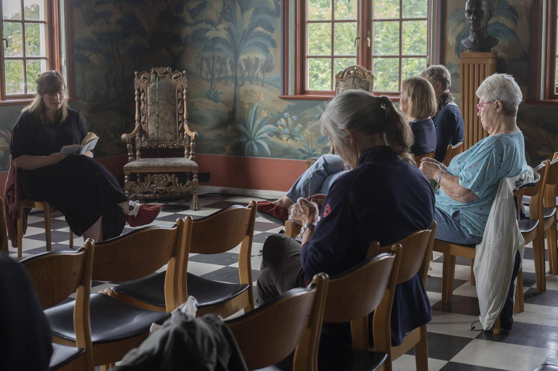 bibliotekar leser, noen kvinner strikker og lytter. I en rokokkosal ved Linderud gård. Foto: Kari M. Sabro