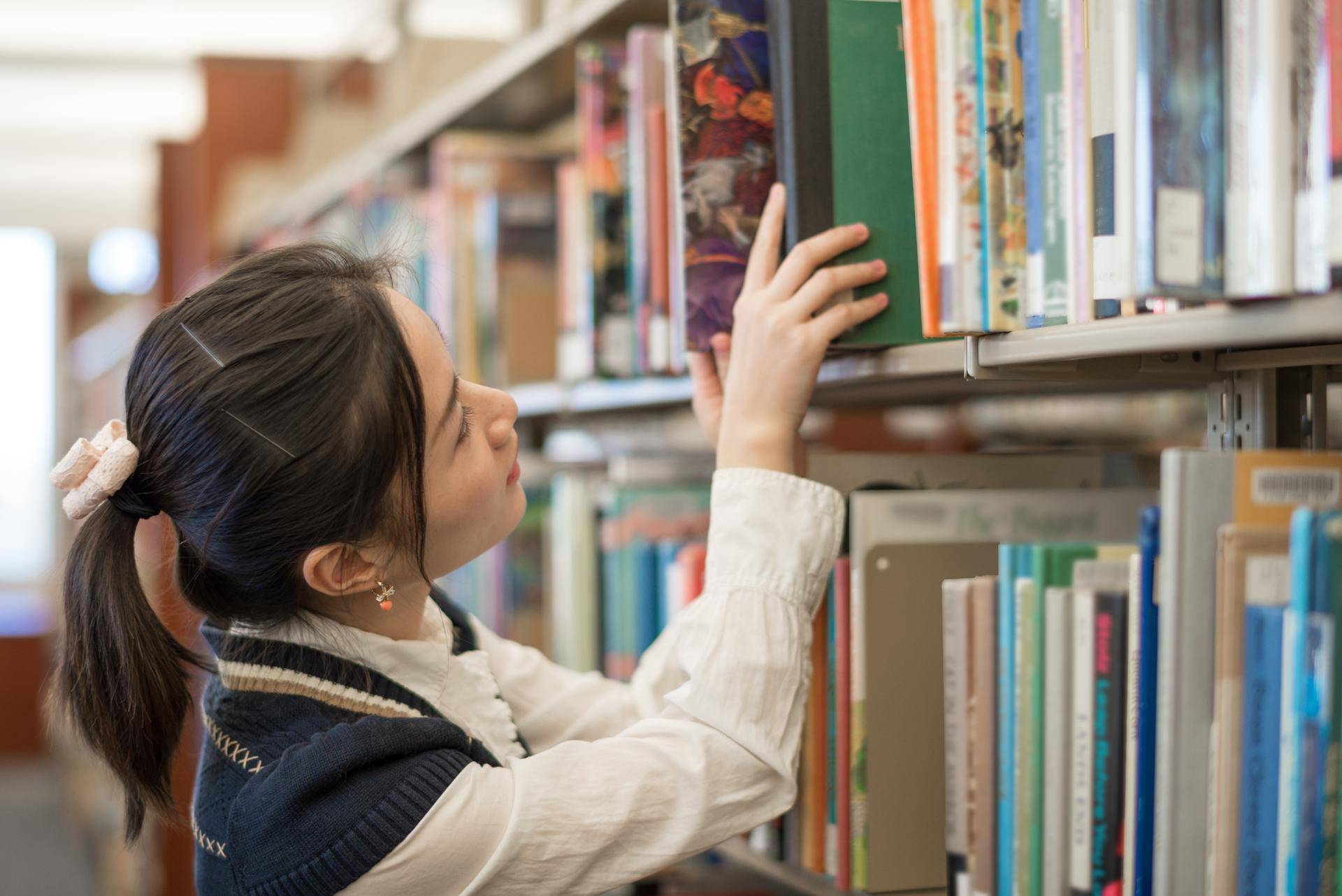 kvinne henter bok fra bokhylle på bibliotek